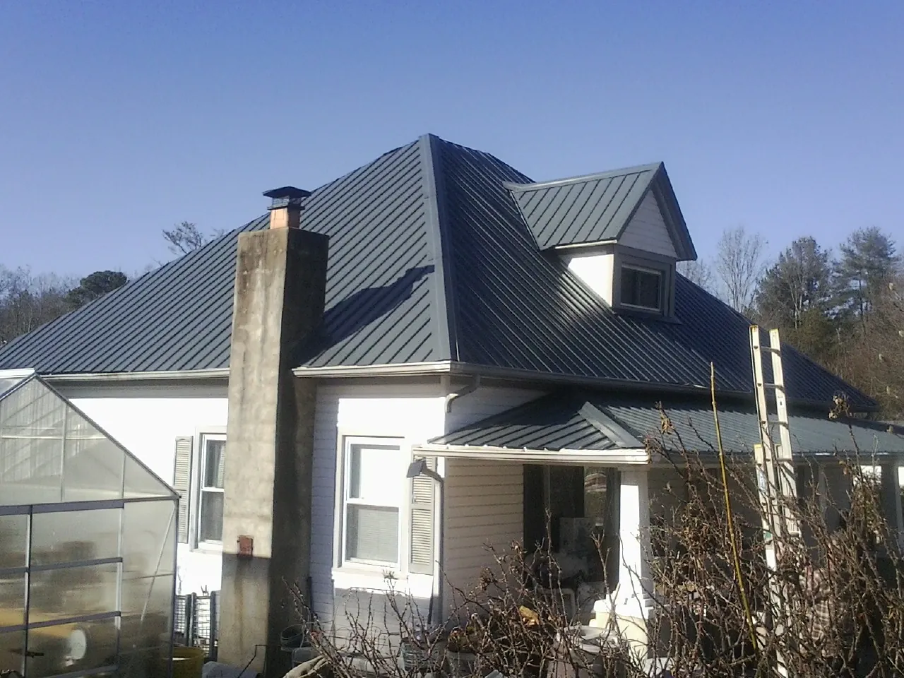 Dark blue standing seam metal roof on a white farmhouse with dormer — Slate & Tile Roof Repair by Roofing Brothers in Newman Grove