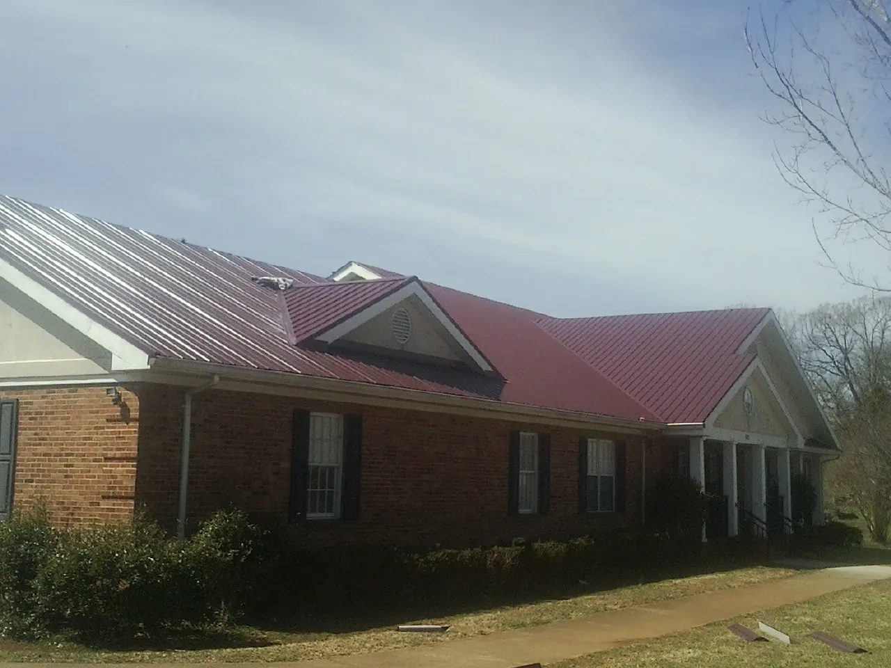 Red metal roof with gabled entries on a long brick building, from a Hail Damage Roof Repair job in Newman Grove
