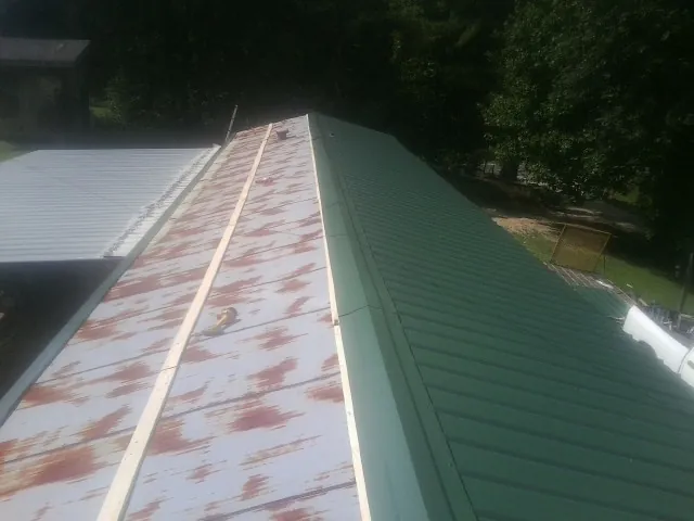 Old rusted panels beside newly installed green metal roofing — Wind Damage Roof Repair by Roofing Brothers in Newman Grove