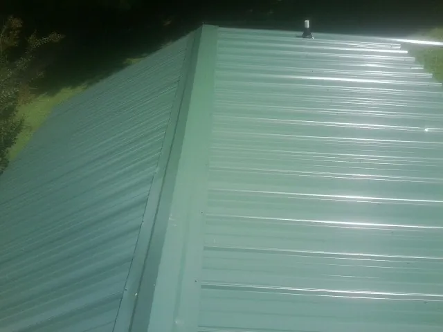 New green metal panels meeting at the ridge of a roof — Flat Roof Repair work by our crew in Newman Grove