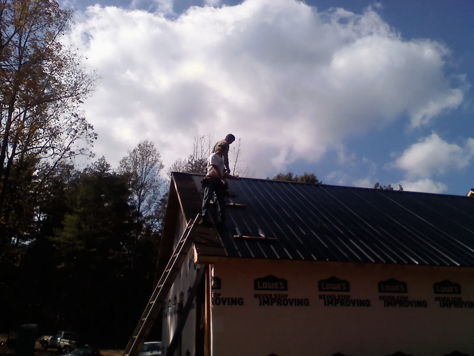 Roofer fastening dark metal panels high against a cloudy sky, from a Roof Inspection job in Newman Grove