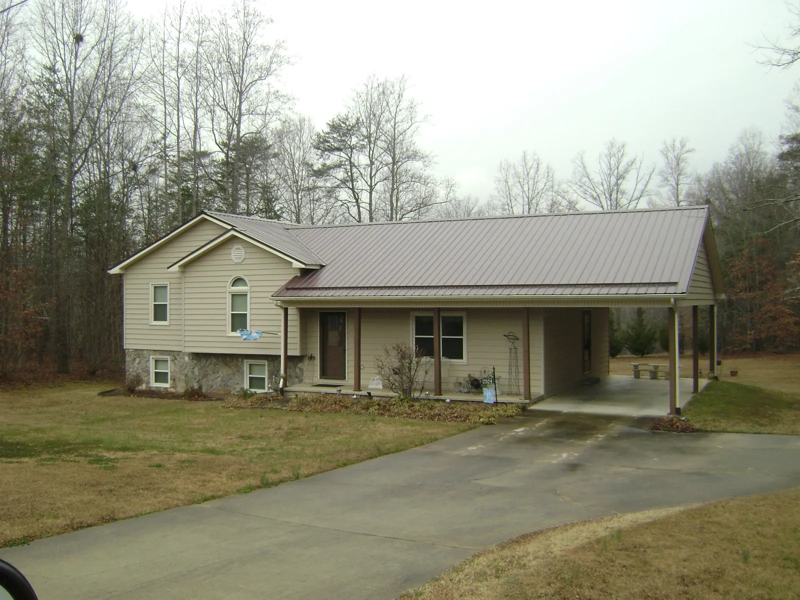 Brown metal roof on a tan split level home with an attached carport in Newman Grove