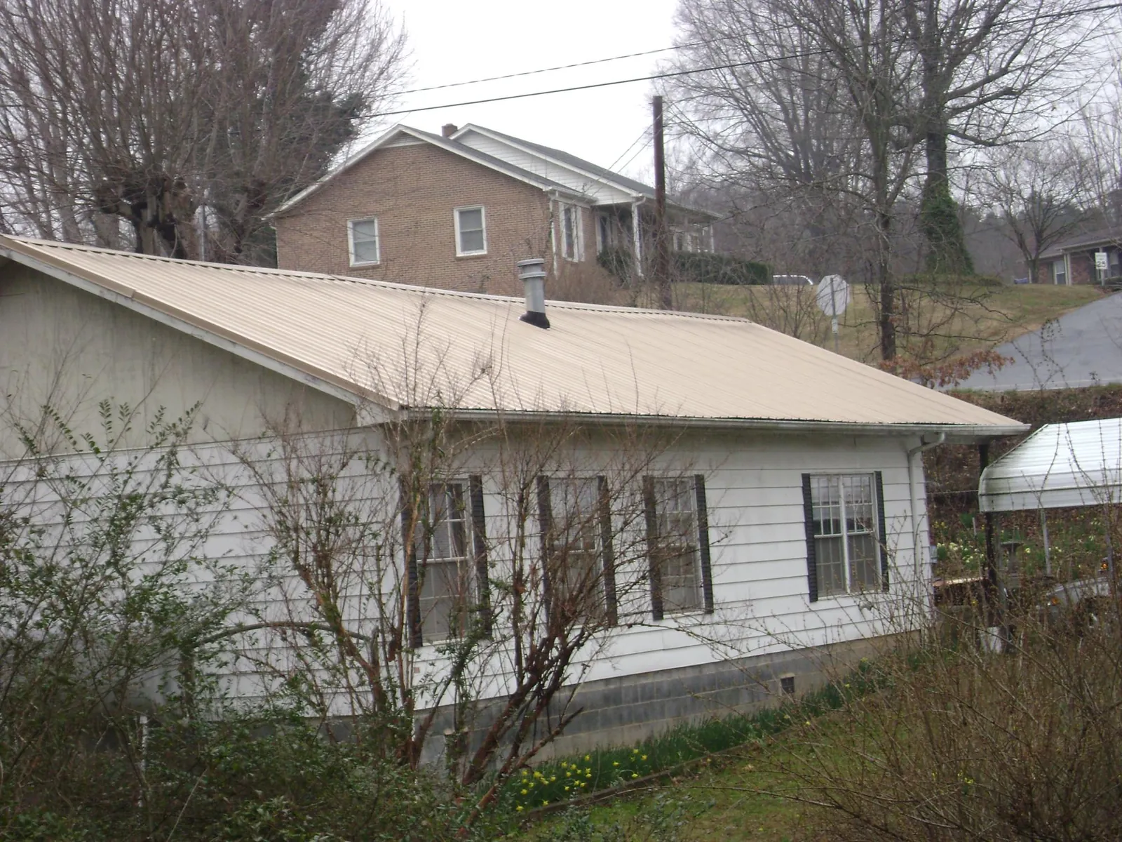 Tan metal roof on a white sided house set into a hillside — Commercial Roofing by Roofing Brothers in Newman Grove