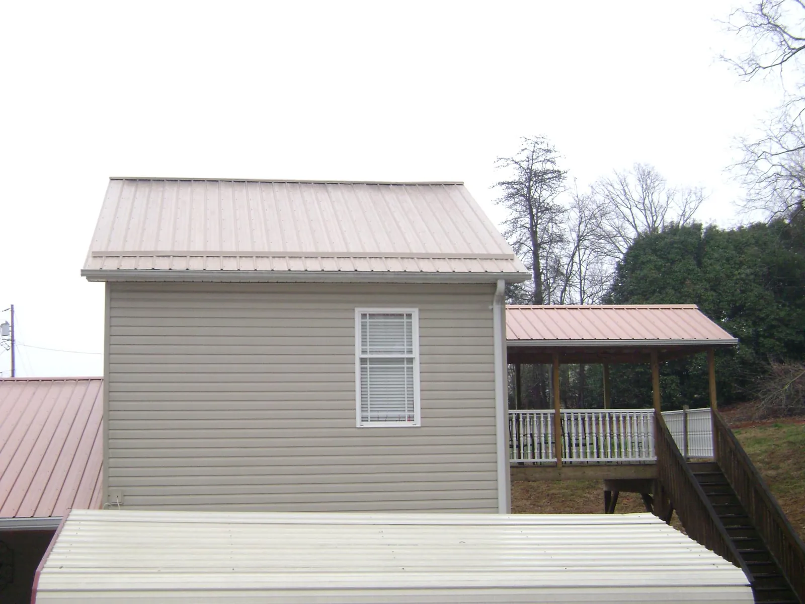 Tan metal roofs on a two story addition and attached porch, from a Roof Replacement job in Newman Grove
